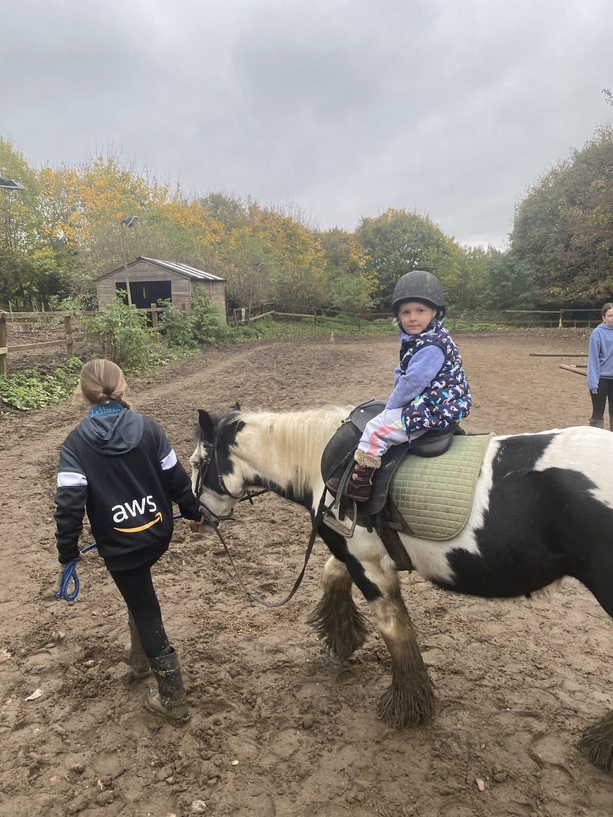 A child being led on a piebald pony in a riding-school arena.